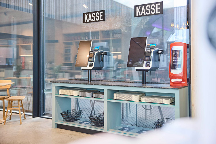 Beim Eintritt authentifizieren sich die Mitarbeiter an einer Zutritts-Stele durch Scan des Firmenausweises. Am Ausgang warten dann zwei Selfcheckout-Kassen auf die Kunden. Foto: Wanzl / Knext
